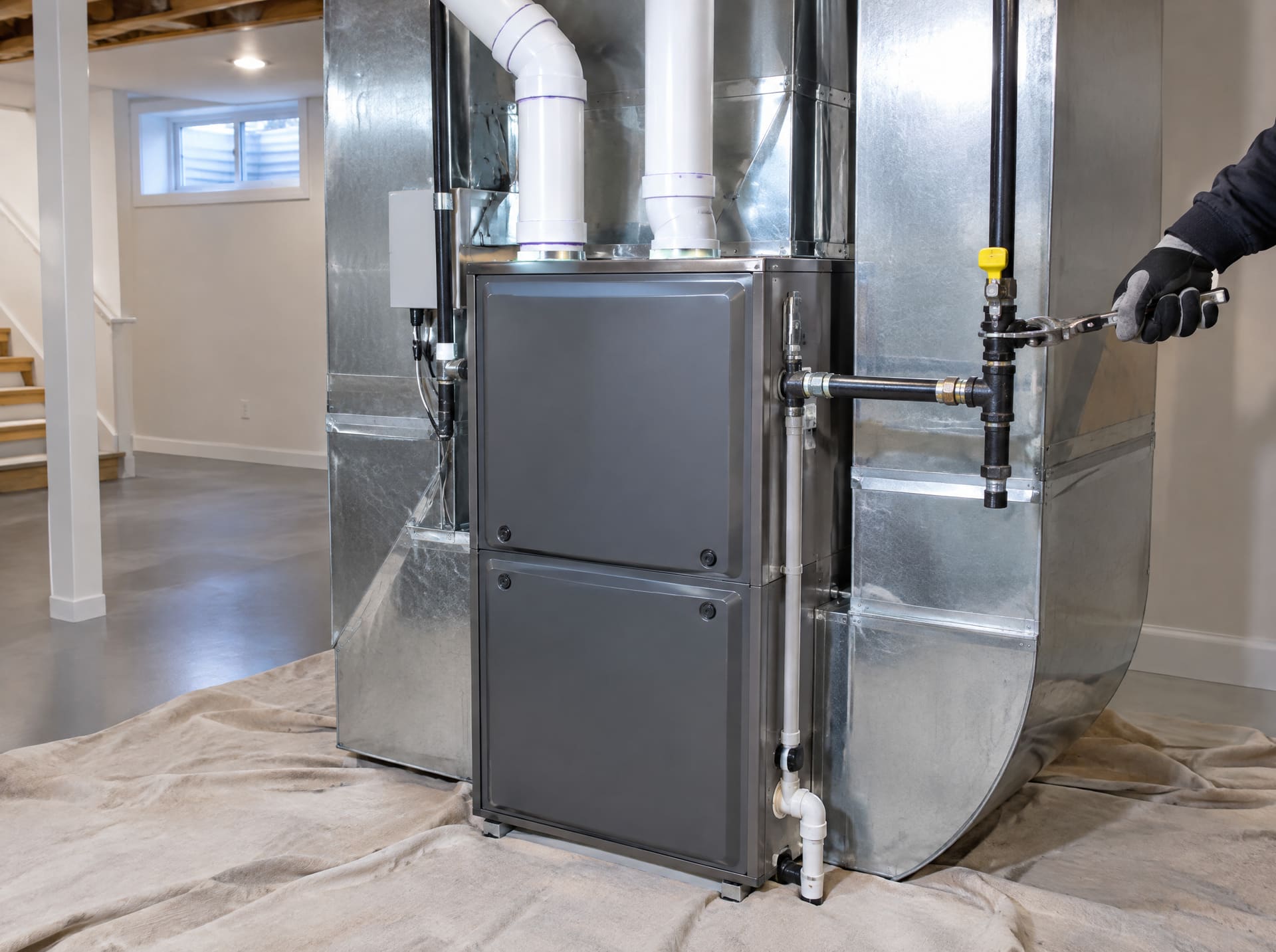A newly installed high-efficiency gas furnace in a finished basement with white PVC venting and new ductwork